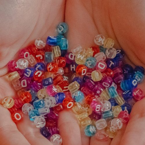 pexels-photo-5933528-5933528 Close-up of vibrant letter beads in hands against a red background, perfect for creative projects.