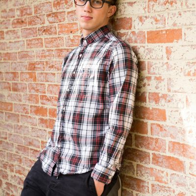 pexels-photo-769732-769732 Stylish young man in casual plaid shirt and eyeglasses leaning against a brick wall.